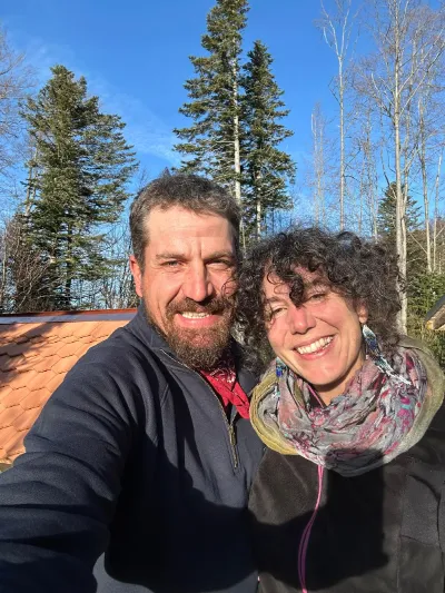 Adeline et Johann au cœur de la nature dans l’environnement d’Adejo.ch Adeline et Johann photographiées en extérieur devant un décor naturel de forêt et de constructions en bois.