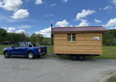 Sauna mobile en bois massif tracté par un véhicule, construction artisanale Adejo Essentiel Bois Sàrl.
