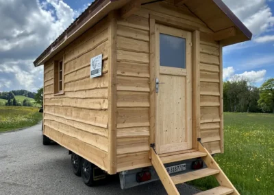 Sauna en bois massif mobile avec escalier d’accès, construit artisanalement par Adejo Essentiel Bois, installé en pleine campagne.