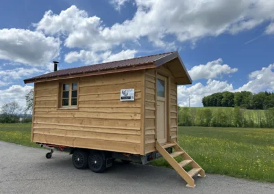 Sauna mobile en bois naturel sur remorque, avec fenêtre latérale et toit à deux pans, réalisé par Adejo Essentiel Bois.