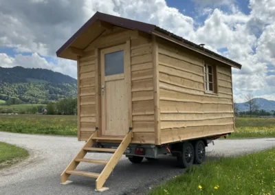 Sauna mobile en bois massif vu de trois quarts arrière, avec escalier et fenêtre, réalisé par Adejo Essentiel Bois Sàrl.