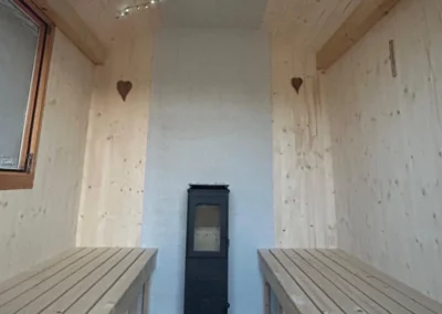 Intérieur d’un sauna en bois Essentiel Bois Adejo Sàrl avec poêle central et bancs en bois