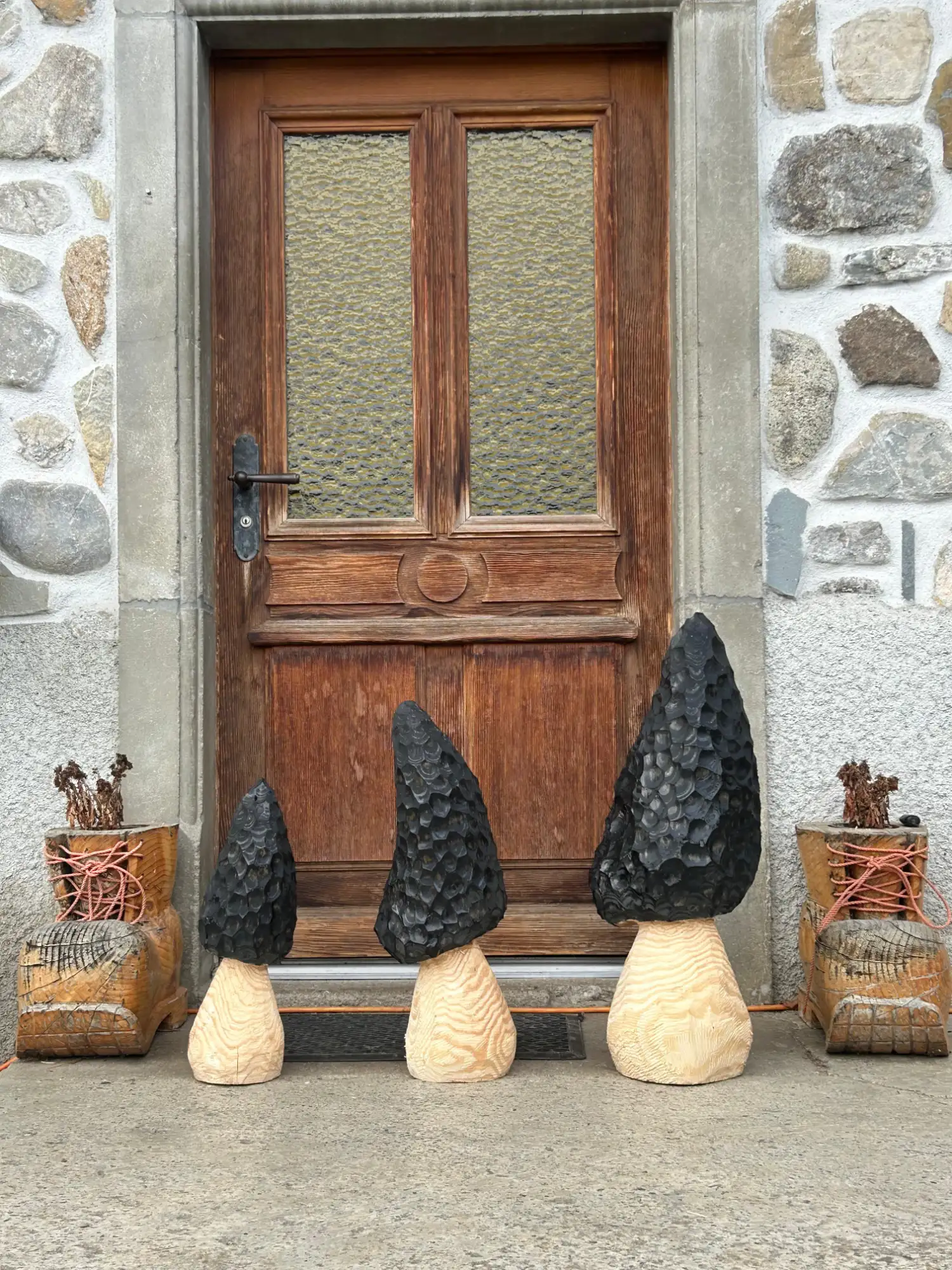 Morilles sculptées en bois brûlé posées devant une porte en pierre – Essentiel Bois Adejo Sàrl