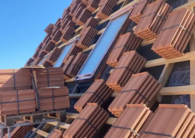 Pose de tuiles sur toiture en cours de construction avec fenêtres de toit – Essentiel Bois Adejo Sàrl